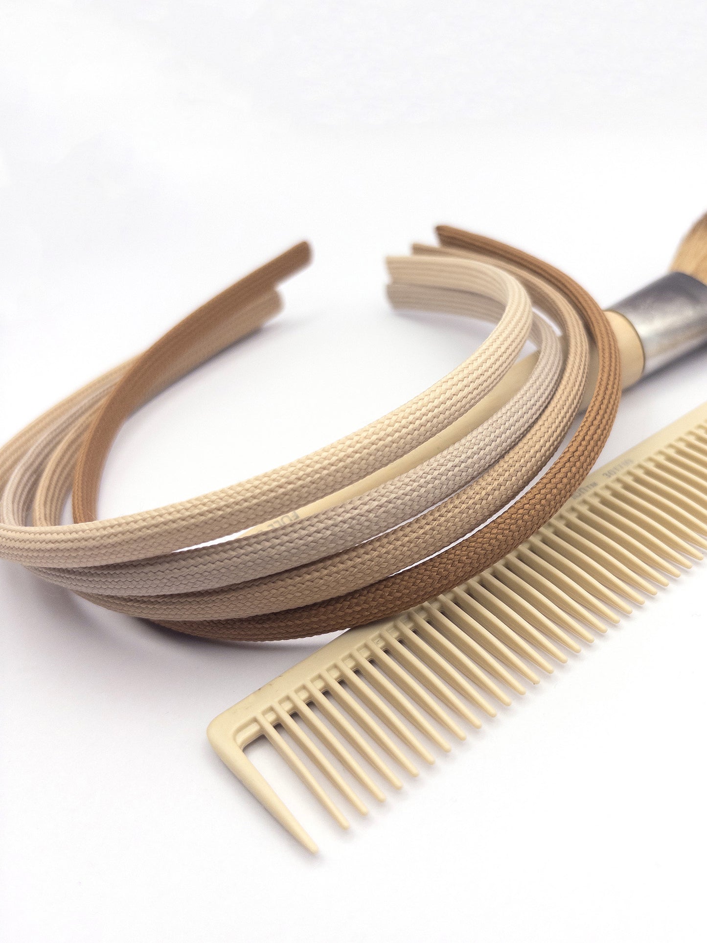 Headbands in 4 shades of cream and blonde laying flat against a makeup brush next to a comb